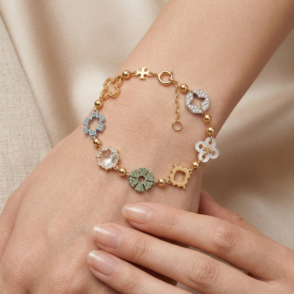A delicate gold-plated bracelet with multiple charm motifs, including floral, geometric, and crystal-studded designs, shown worn on a woman's wrist.
