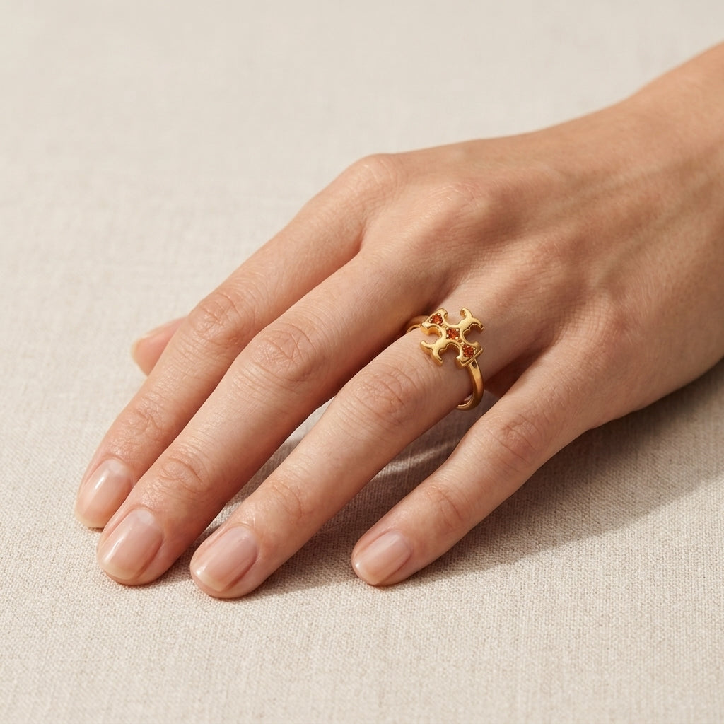 A gold ring with a textured, organic floral or honeycomb-like top, shown worn on a person's ring finger against a neutral beige fabric background.