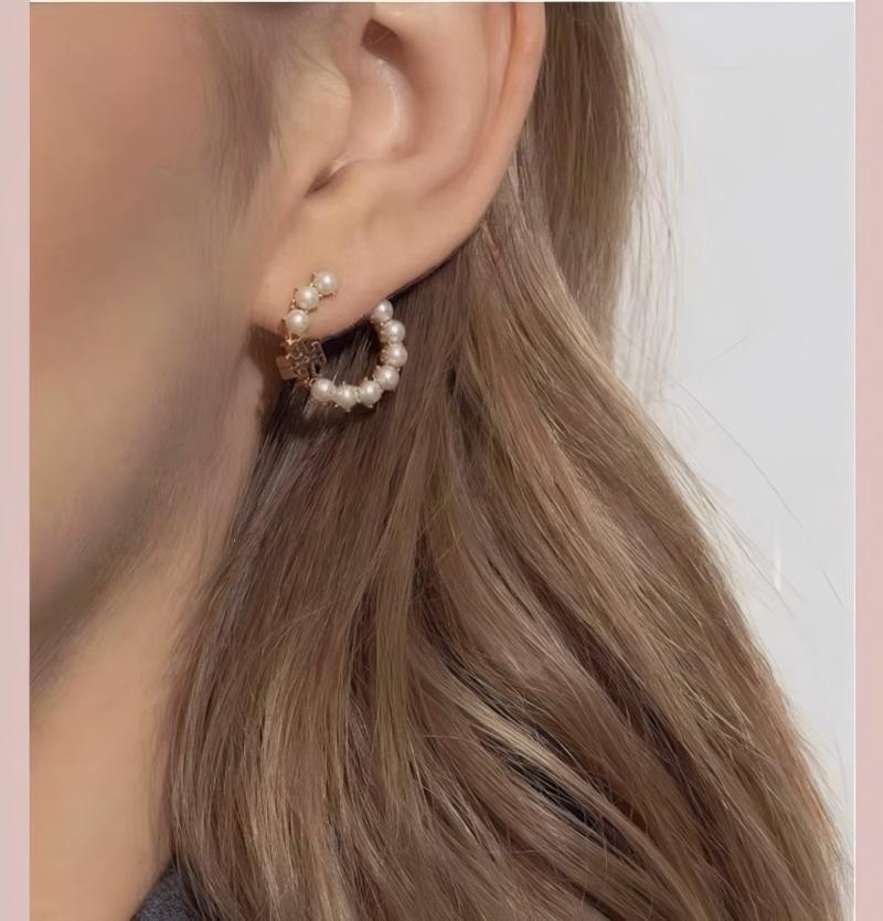 A confident North American woman in casual chic attire (e.g., a sweater and jeans) smiling, with a clear focus on her ear wearing the Kira earrings. Natural daylight setting.