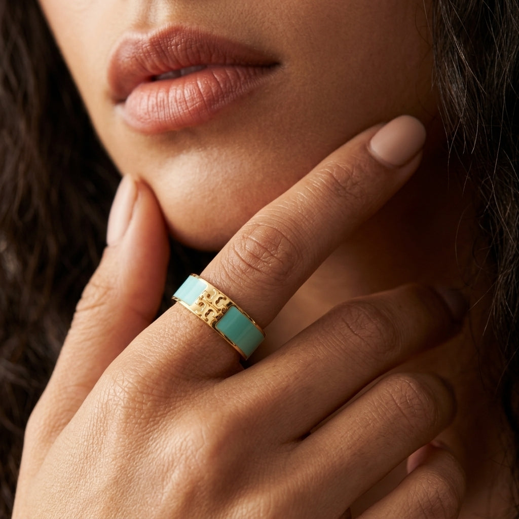 A close-up of a model's hand wearing a gold ring with a turquoise blue inlay, resting near her chin.
