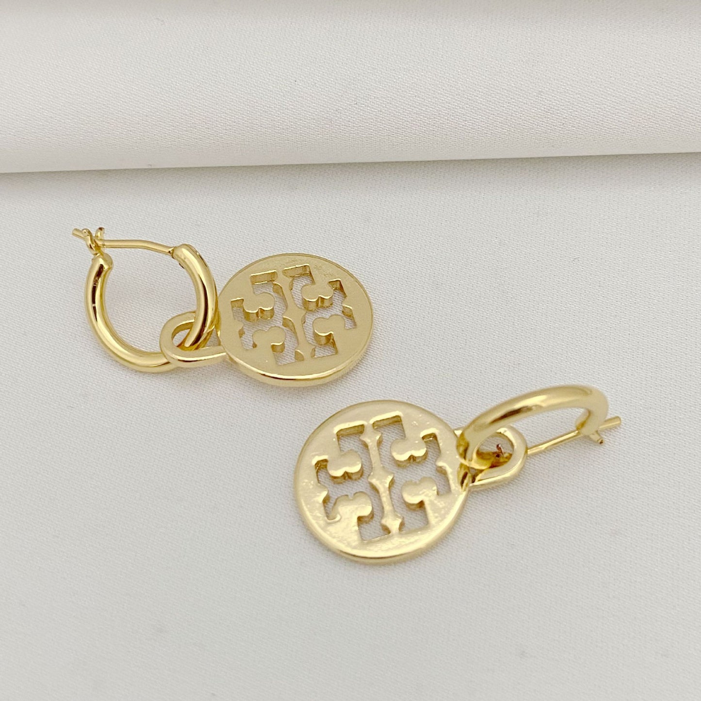 Gold hoop earrings with intricate designs on a light gray background