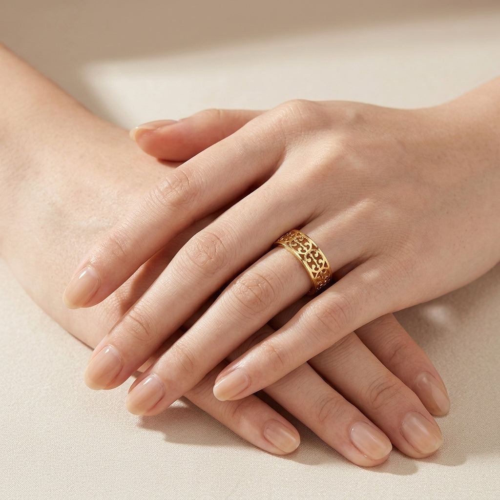 A close-up of crossed hands wearing a textured gold ring with an openwork geometric pattern, set against a soft beige background.