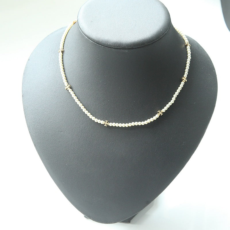 A delicate necklace made of small white beads with small gold decorative accents, displayed on a matte black jewelry bust against a white background.