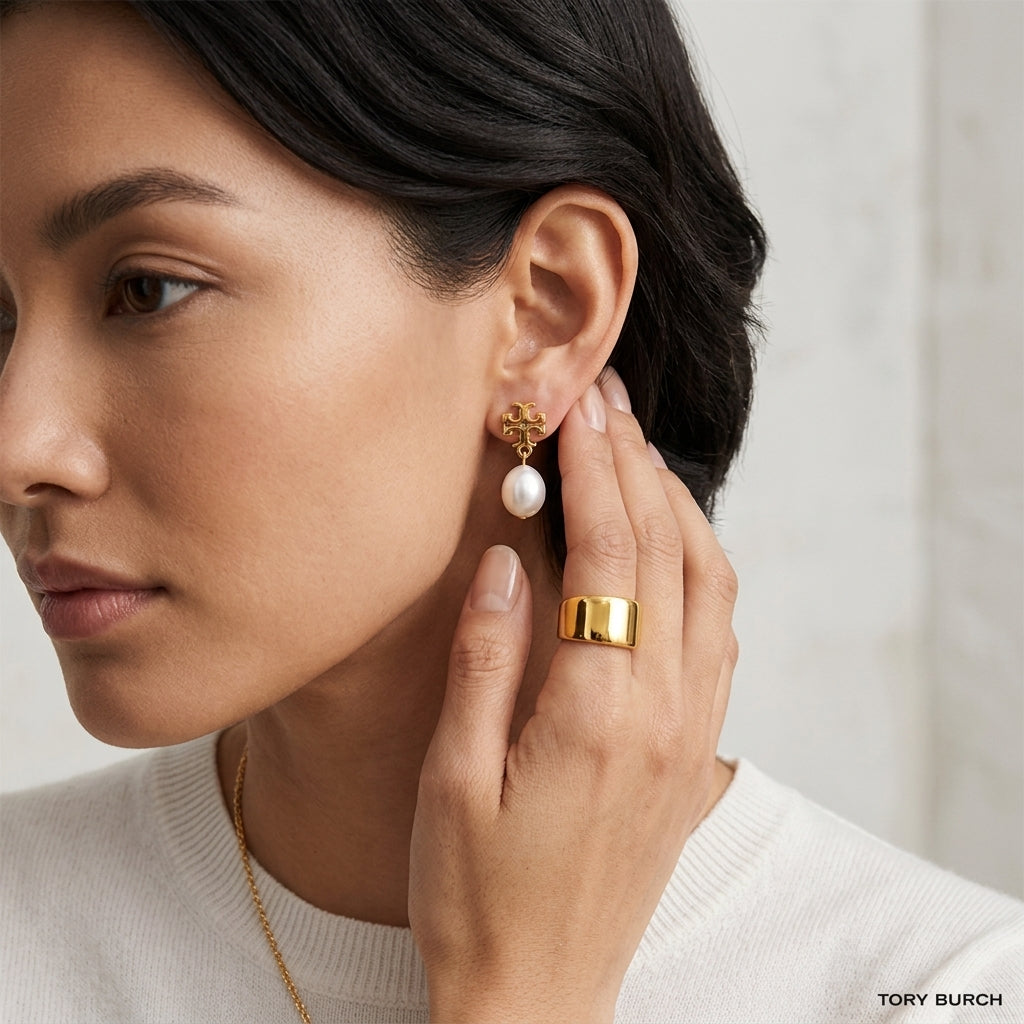 Woman wearing a gold ring and pearl earring with a neutral background