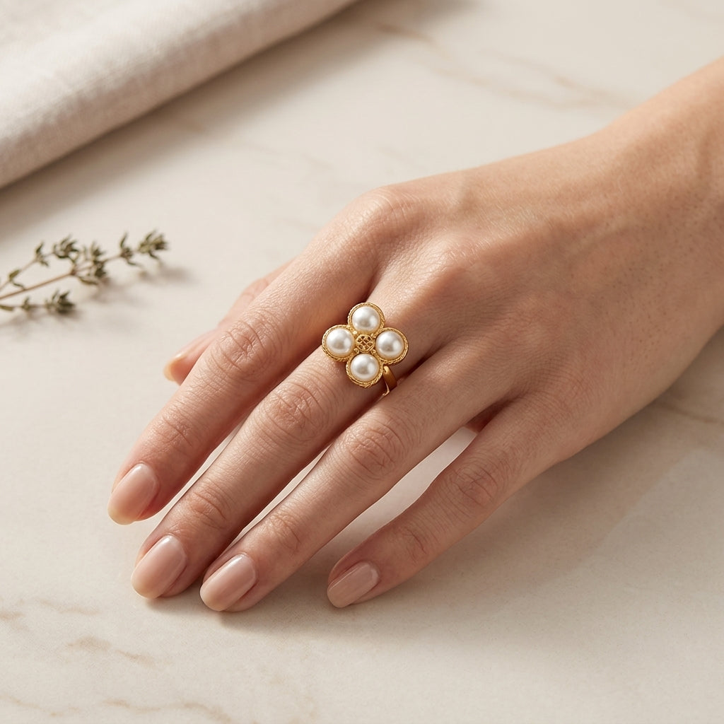 A gold ring with five white pearl-like beads arranged in a flower shape, worn on a woman's finger against a light marble background.