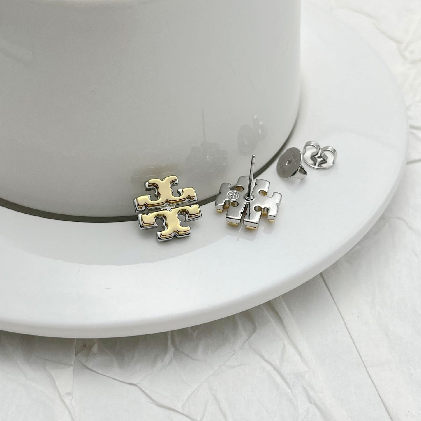 Clean grid of individual stud pairs, each clearly showing design details like logo engraving, pearl luster, or crystal sparkle.