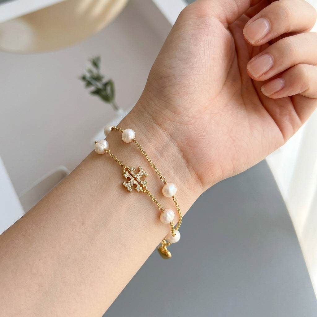 A close-up of a person's wrist wearing two delicate gold chain bracelets. One bracelet features small white pearl beads, and the other has a small gold cross charm and a tiny gold crescent moon pendant.