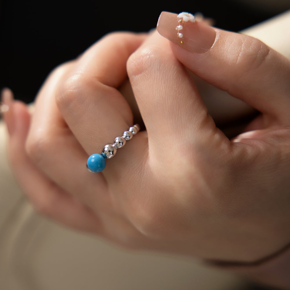 Close-up of a hand wearing a ring with blue and silver beads on a blurred background