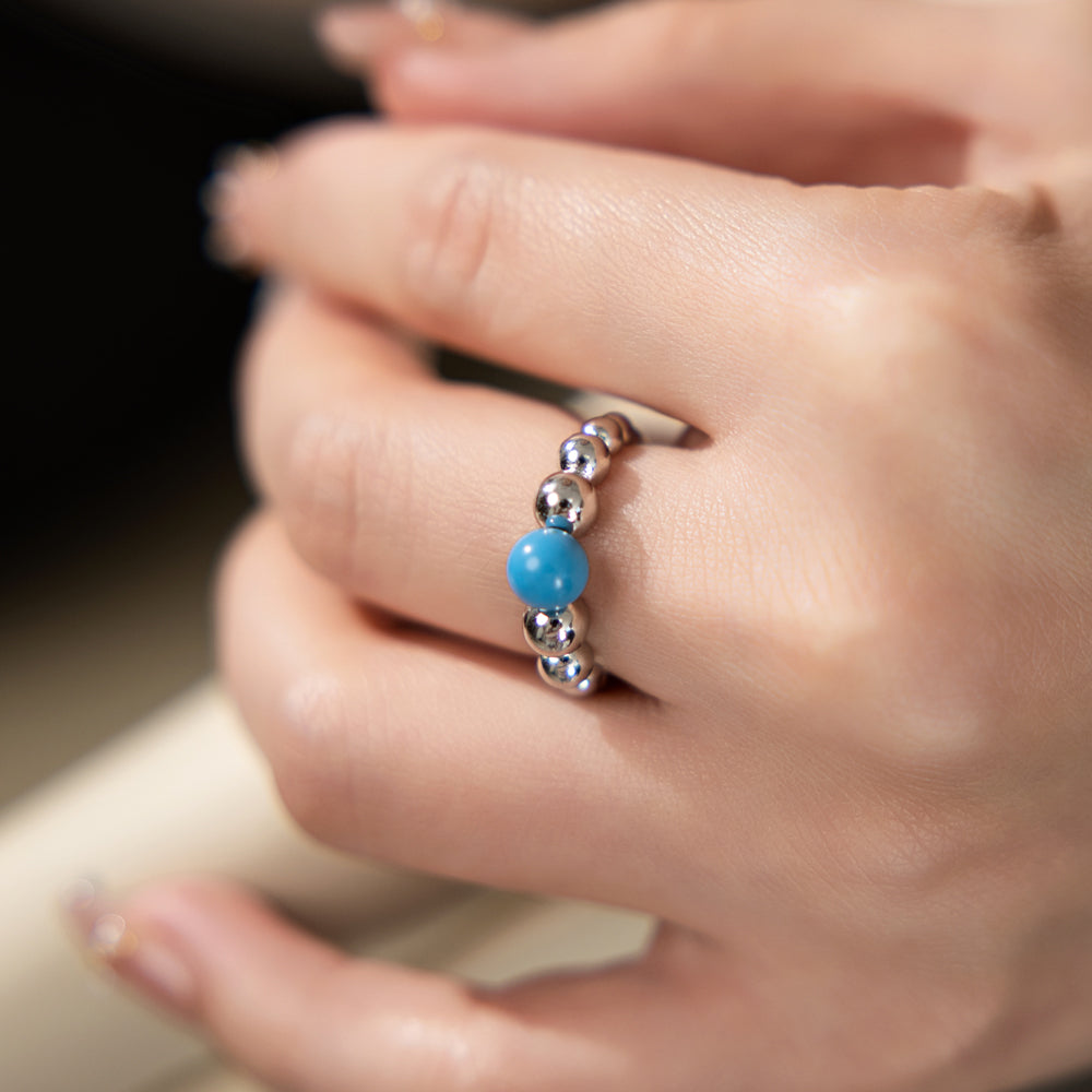 Close-up of a hand wearing a ring with blue and silver beads.