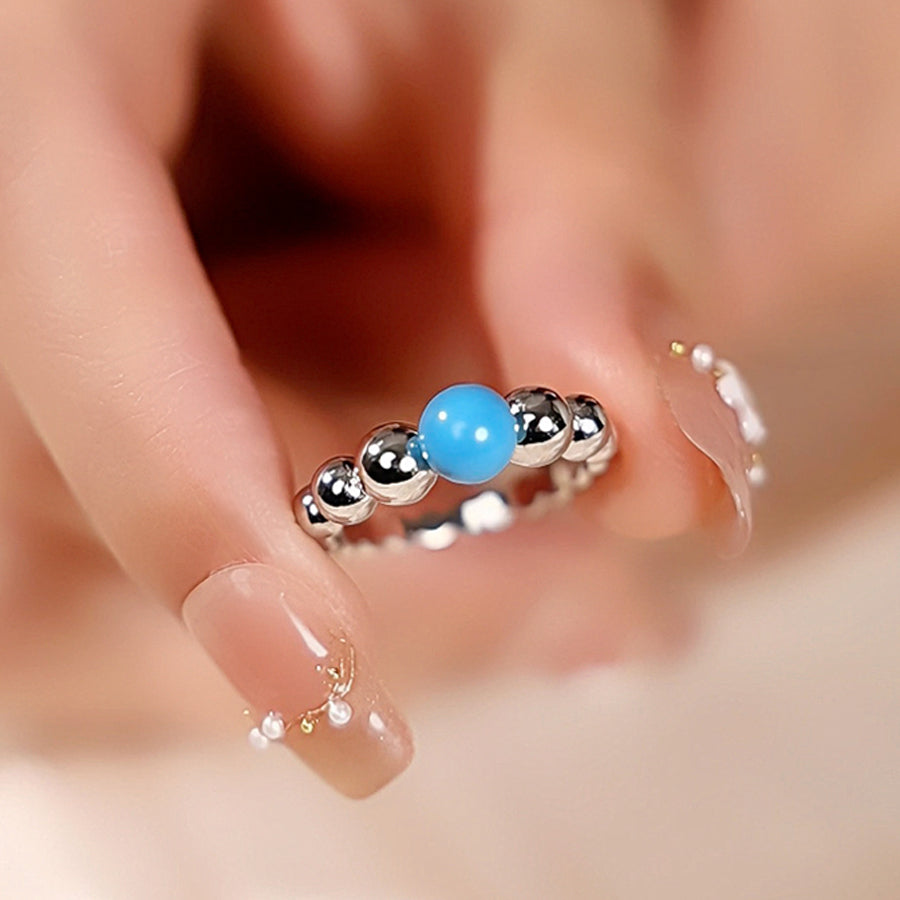 Close-up of a silver earring with a blue bead worn by a person.