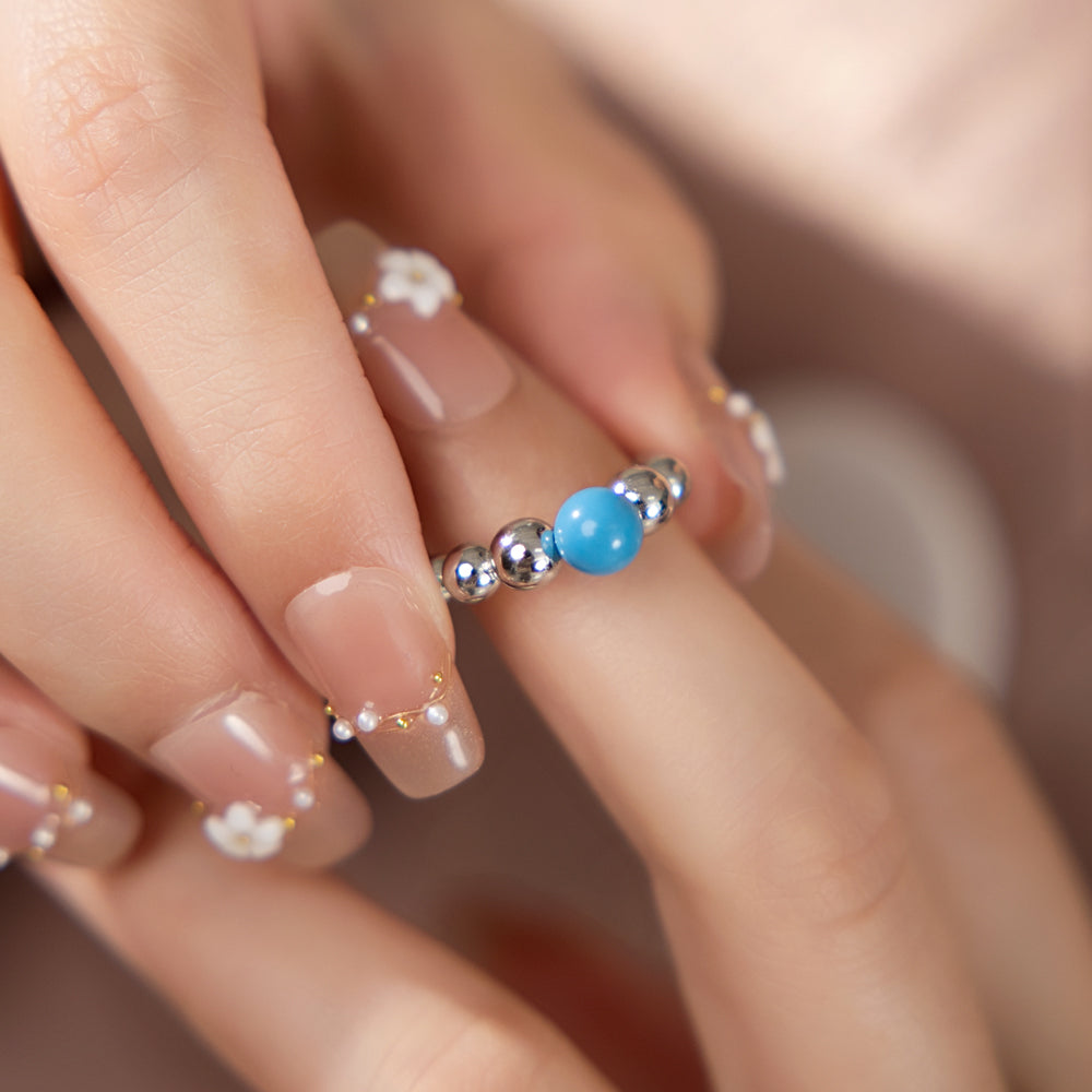 Close-up of a hand wearing a ring with blue and silver beads on a blurred background