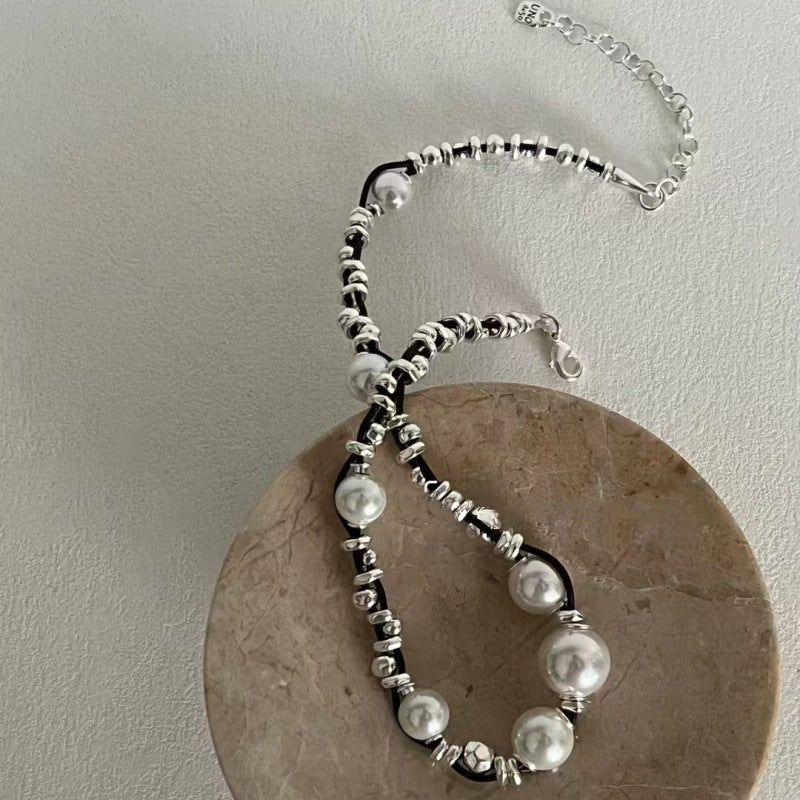 A beaded necklace with large white pearls and silver-toned spacer beads, draped over a round beige stone display on a light gray wall.