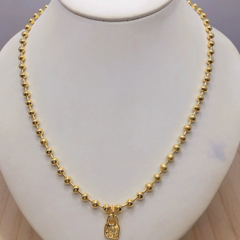 A gold beaded necklace with a small hanging elephant charm, displayed on a white neck mannequin bust.