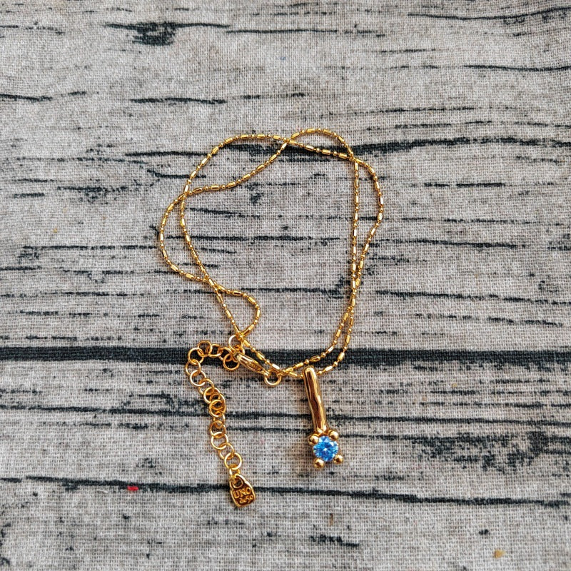 Gold necklace with a blue gemstone pendant on a textured gray background