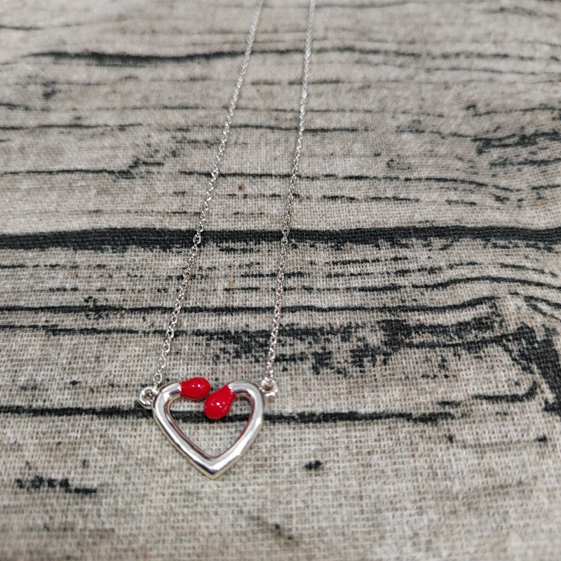A silver open heart pendant necklace with two small red heart charms, displayed on a textured gray fabric background.
