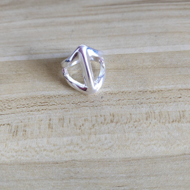 A polished silver geometric ring with an abstract triangular design, resting on a light-colored wooden surface.