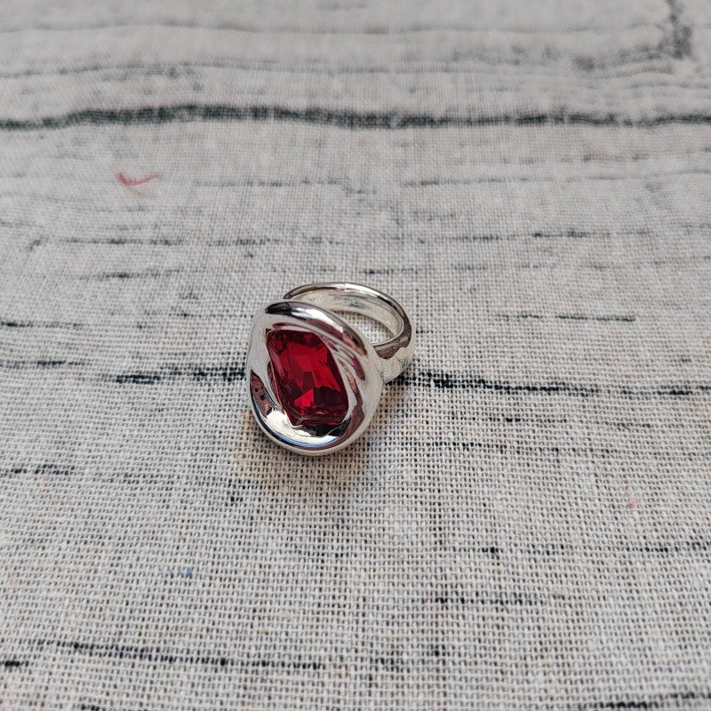 A silver ring with a large, polished teardrop-shaped red gemstone, resting on a textured gray woven fabric background.