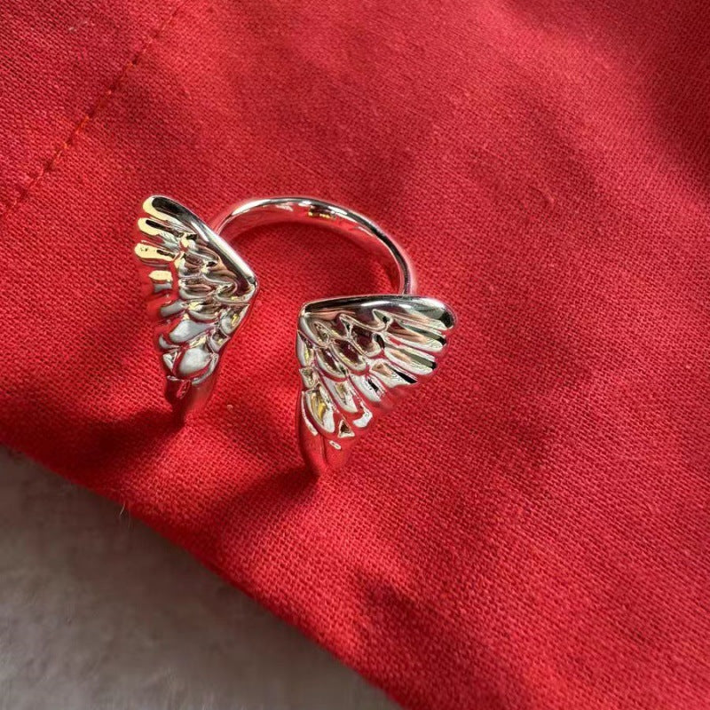 A silver-toned wing-shaped ring resting on a textured red fabric background.