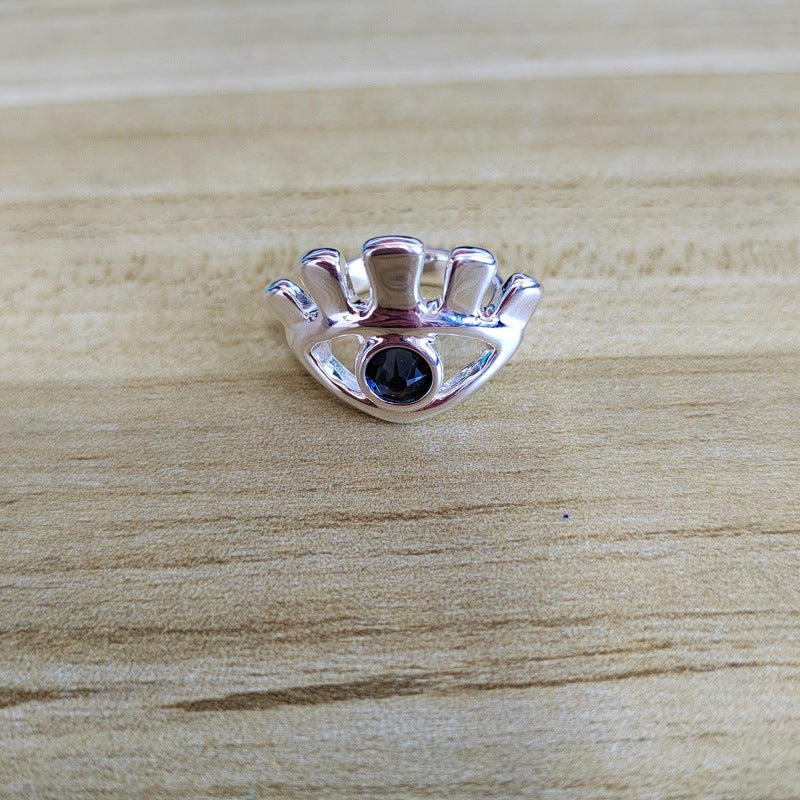 A silver crown-shaped ring with a central round black gemstone, resting on a light wood grain surface.