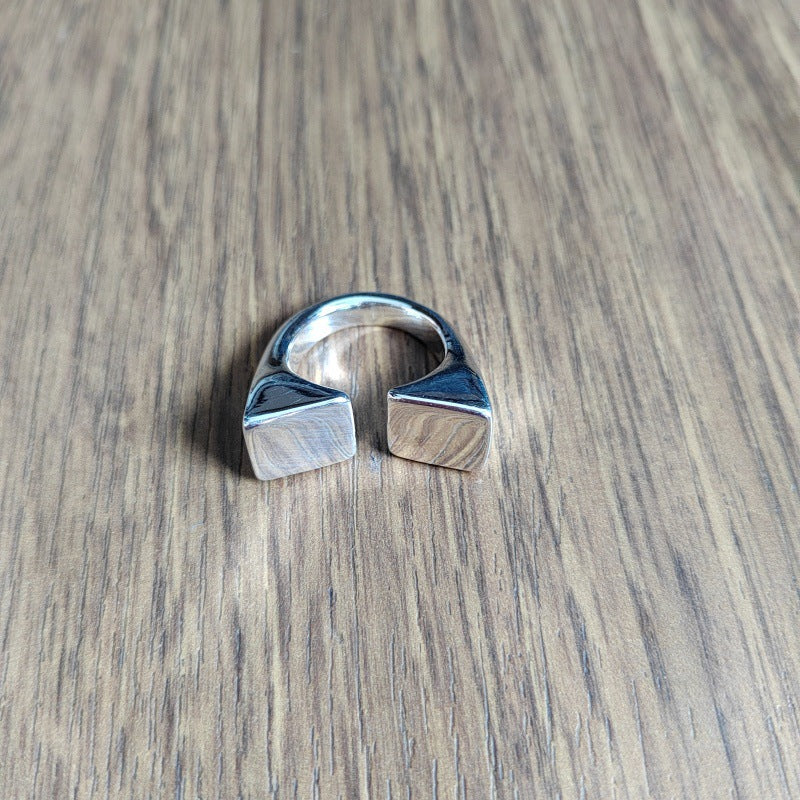 A silver-toned open ring with two square, beveled ends, resting on a brown wood-grain surface.
