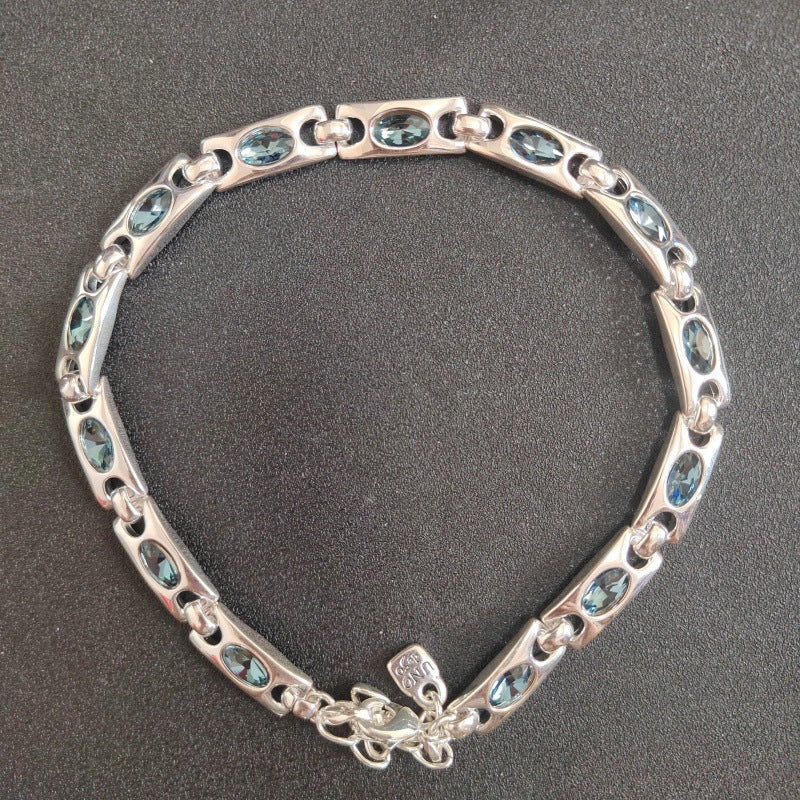 A silver-toned link bracelet featuring oval and marquise-cut light blue gemstones, displayed on a dark textured background.