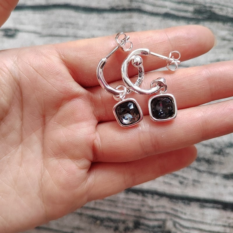 Silver earrings with dark gemstones held in a hand against a marble background