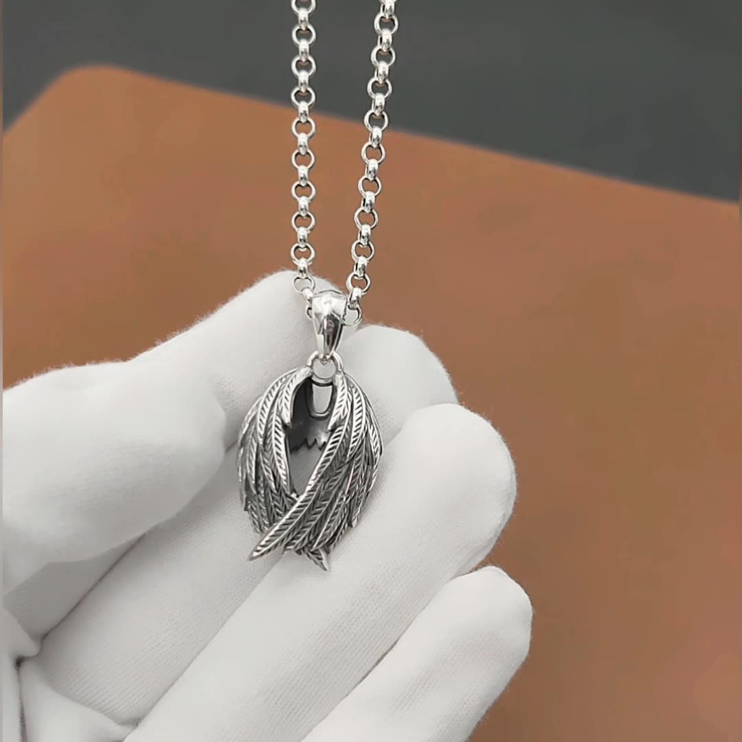 Silver necklace with a feather pendant held by a gloved hand against a blurred background