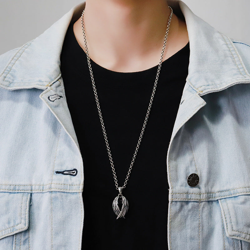 Person wearing a long silver necklace with a pendant, dressed in a light blue denim jacket over a black shirt.
