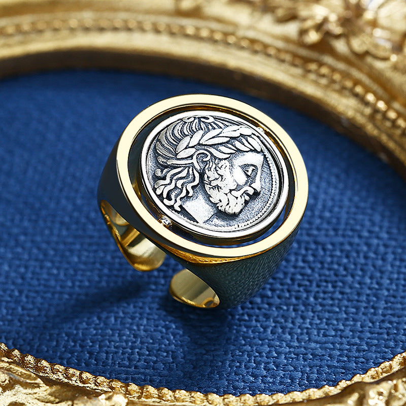 Gold ring with a silver coin featuring a face design on a blue fabric background