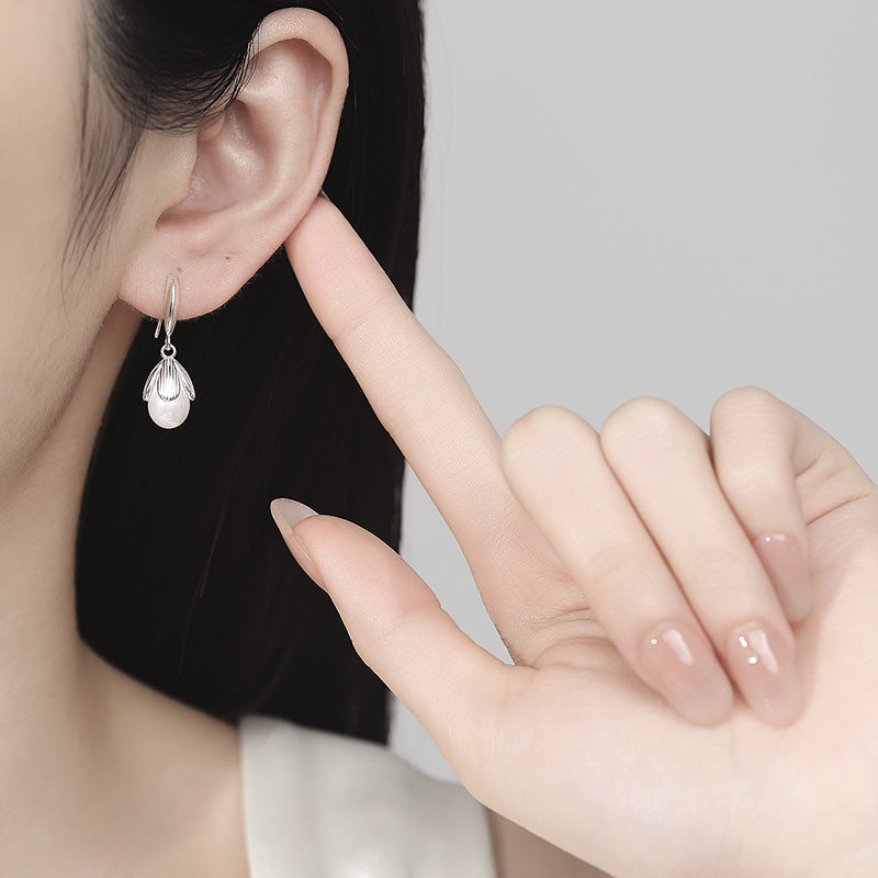 Silver teardrop earring being pointed to by a hand against a neutral background