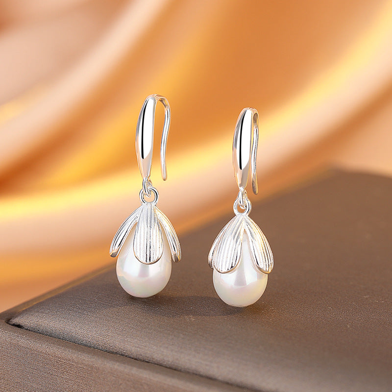 Pearl earrings with silver teardrop designs on a soft fabric background