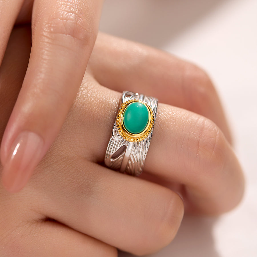 Silver ring with a green gemstone on a finger against a neutral background