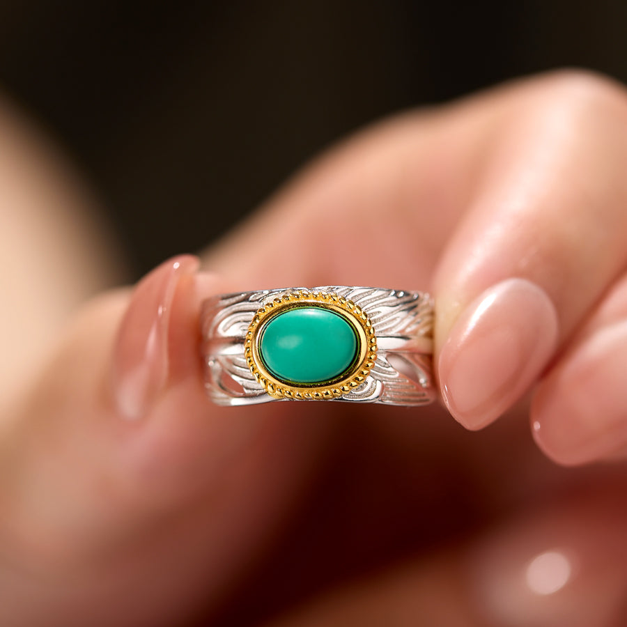 Silver ring with a turquoise stone held between fingers against a blurred background