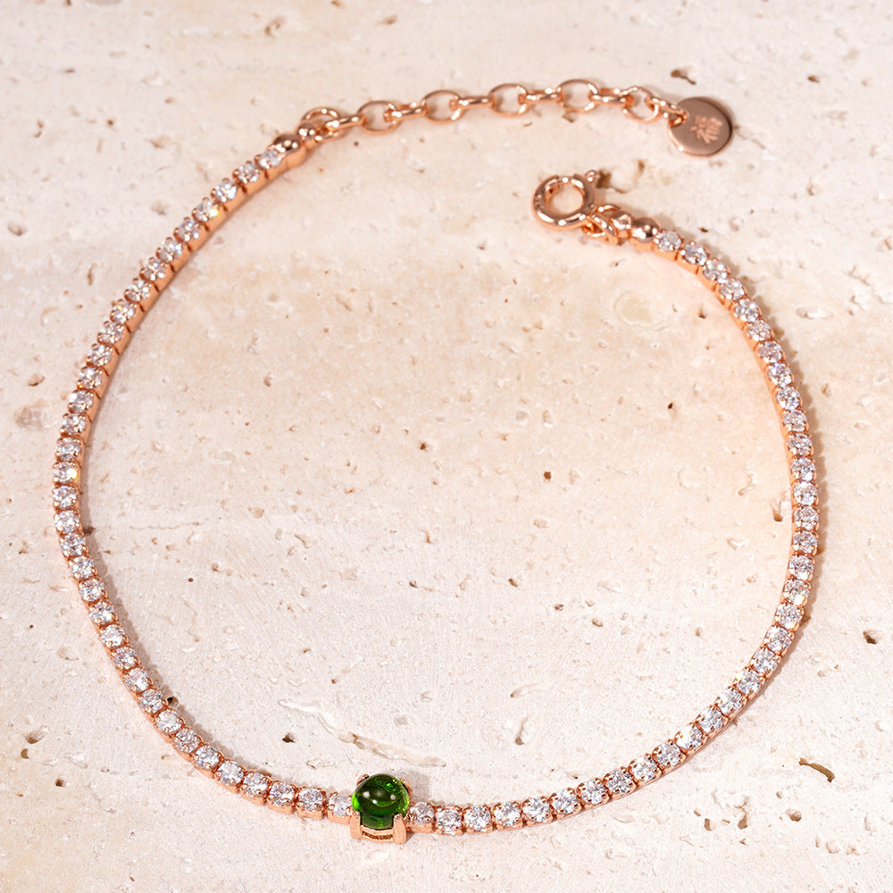 Rose gold bracelet with green gemstone on a beige background