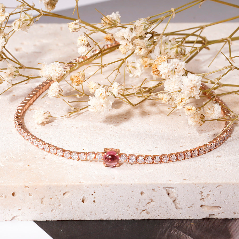 Rose gold bracelet with a pink gemstone on a marble surface with dried flowers.