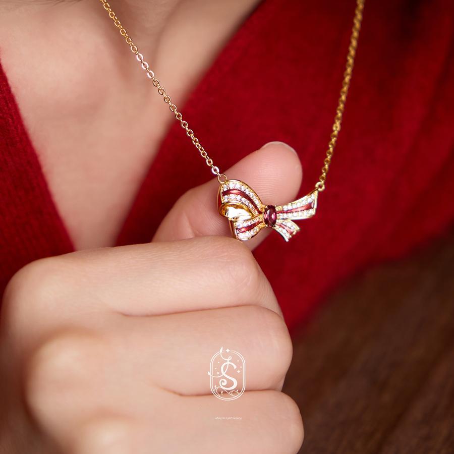 Gold bow-shaped necklace held by a hand against a red background