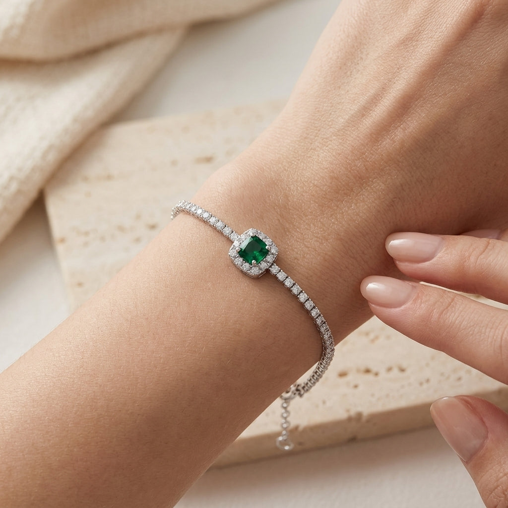 Side angle view of a model wearing an elegant cushion emerald halo bracelet resting on a beige stone surface.
