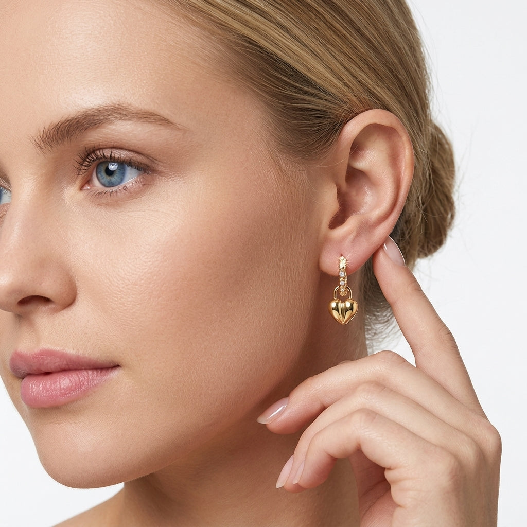 Model wearing gold puffed heart lock dangle huggie hoop earrings in a studio lifestyle portrait.