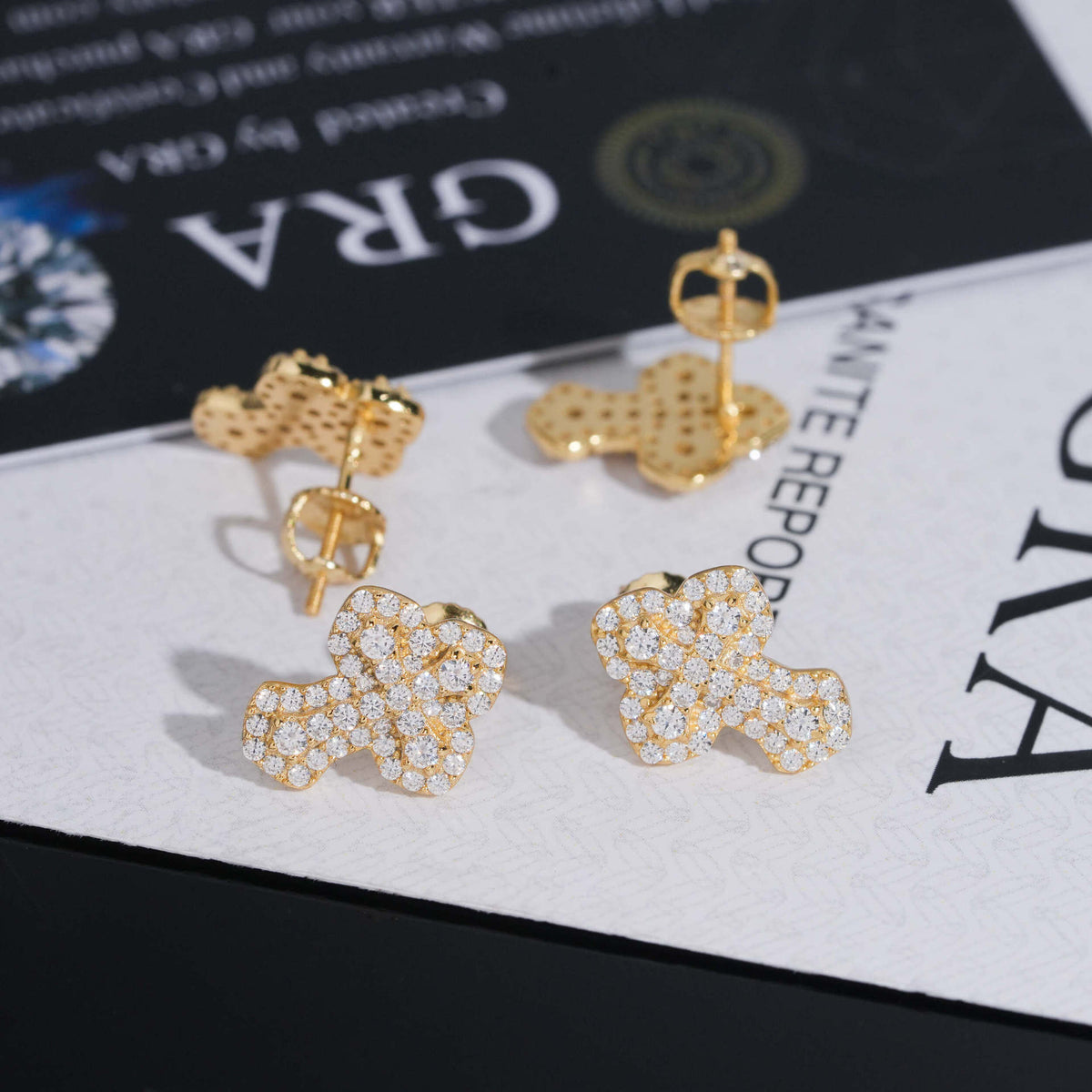 Yellow gold iced out clover floral micro-pave moissanite stud earrings displayed on GRA report card