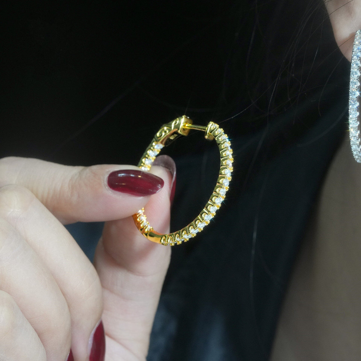 Close-up of hand holding yellow gold iced out eternity moissanite hoop earring near ear