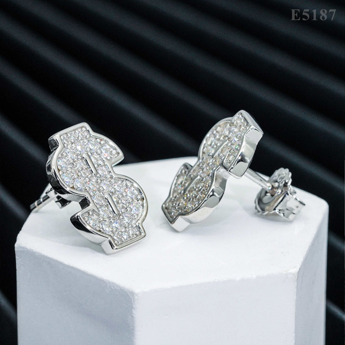 Pair of silver iced out money sign dollar sign moissanite stud earrings on white pedestal box