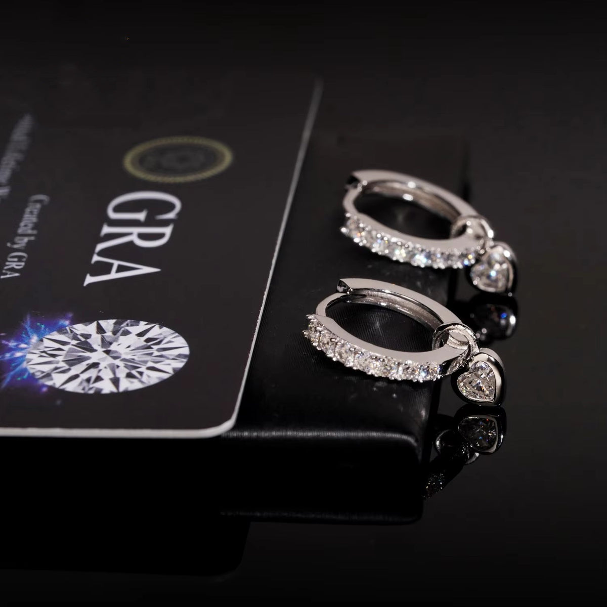 Silver iced out huggie hoop moissanite earrings showing open hinged mechanism and removable pink heart charm
