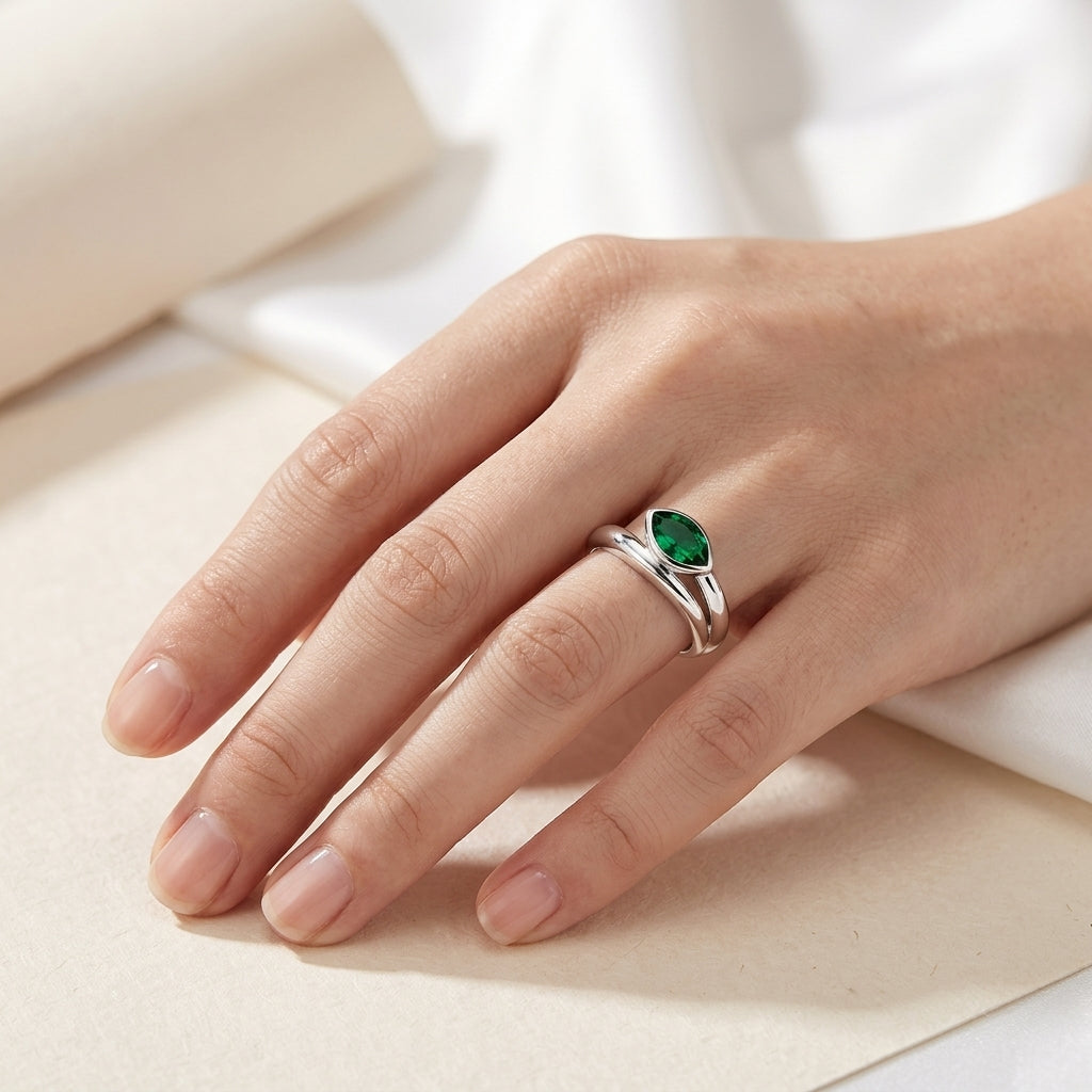 Side angle lifestyle shot of a model showcasing a minimalist marquise-cut emerald bypass engagement ring on her finger.