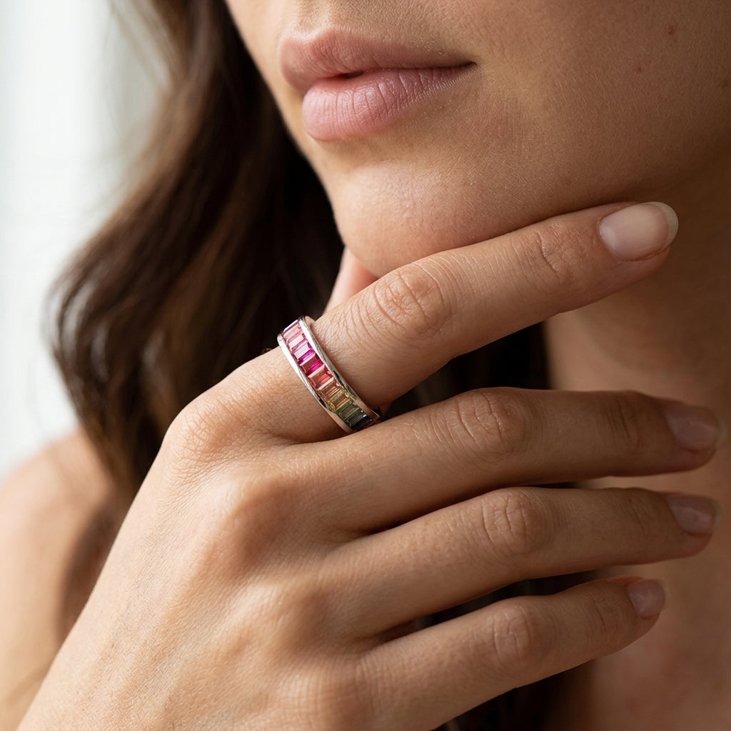 Model holding hand near chin wearing rainbow baguette cut gemstone channel eternity band.