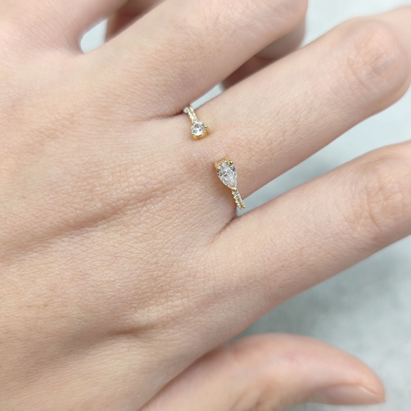 Gold ring with a diamond on a person's finger against a neutral background