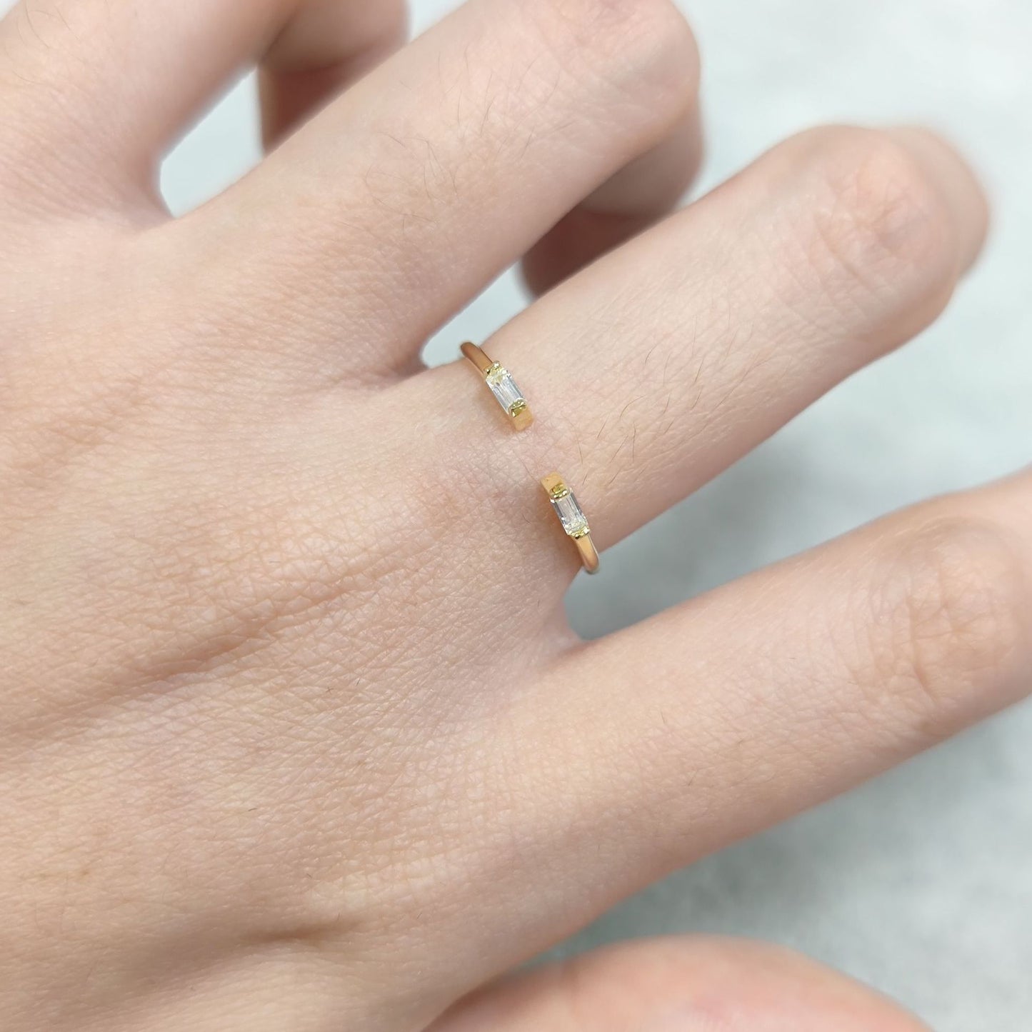Two gold rings with small stones on a person's finger against a neutral background