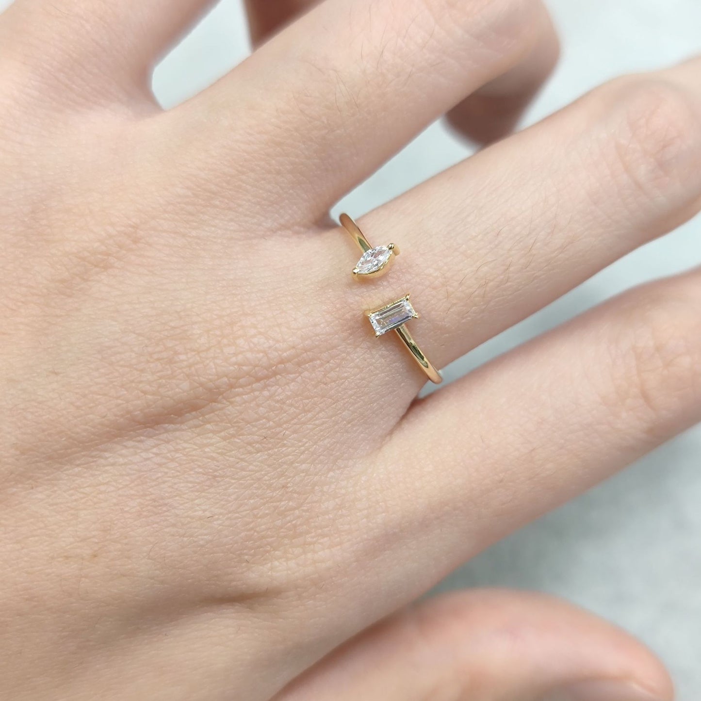 Gold ring with a diamond on a person's finger against a neutral background