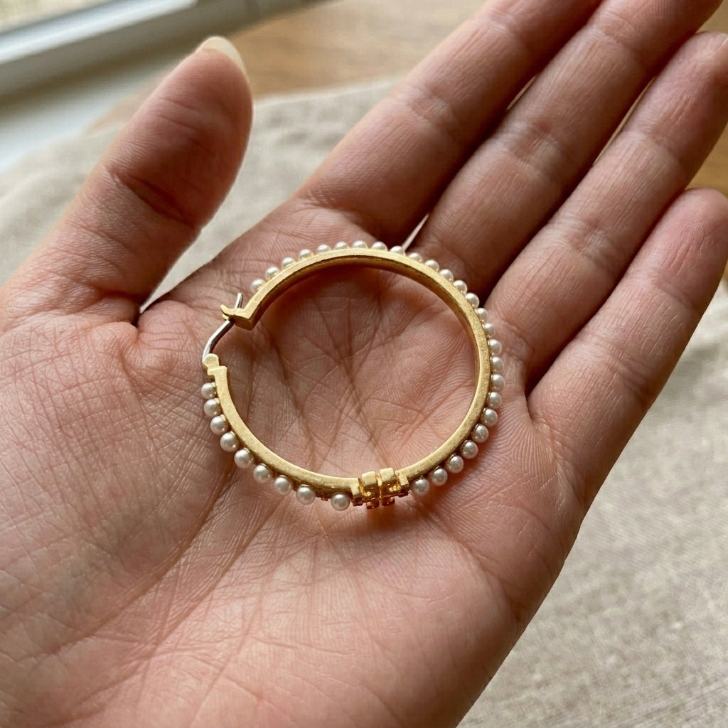 Hand-held scale reference of Tory Burch Double T Pearl Hoops to show the hoop diameter and pearl size
