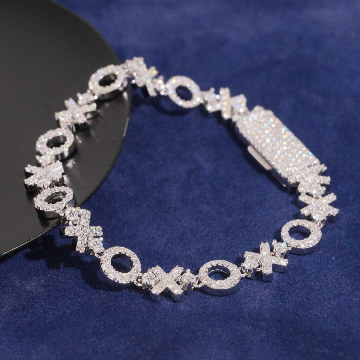 Top-down angled view of XOXO moissanite tennis bracelet on blue fabric.