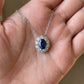 Close-up held in hand, 0.8ct oval blue sapphire pendant necklace featuring halo setting.